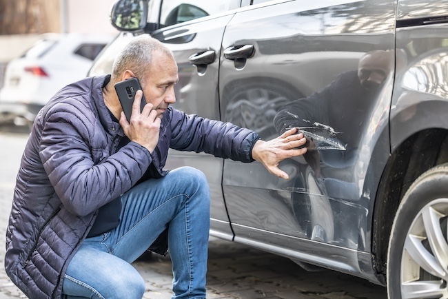 man on the phone checking his car for accident damage while on the phone with a top-rated car accident lawyer.